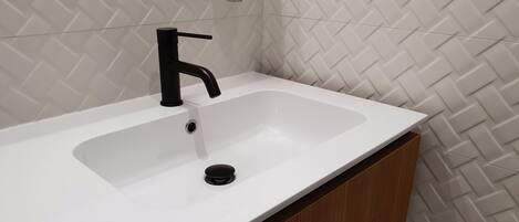 A modern bathroom with a white sink, black faucet, and a diamond-patterned tiled wall.
