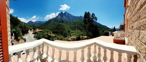 A balcony with a view of a mountainous landscape, a road, and residential buildings.