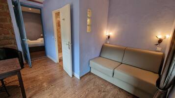 Een kamer met een houten vloer, een beige bank, een witte deur en een bakstenen muur.