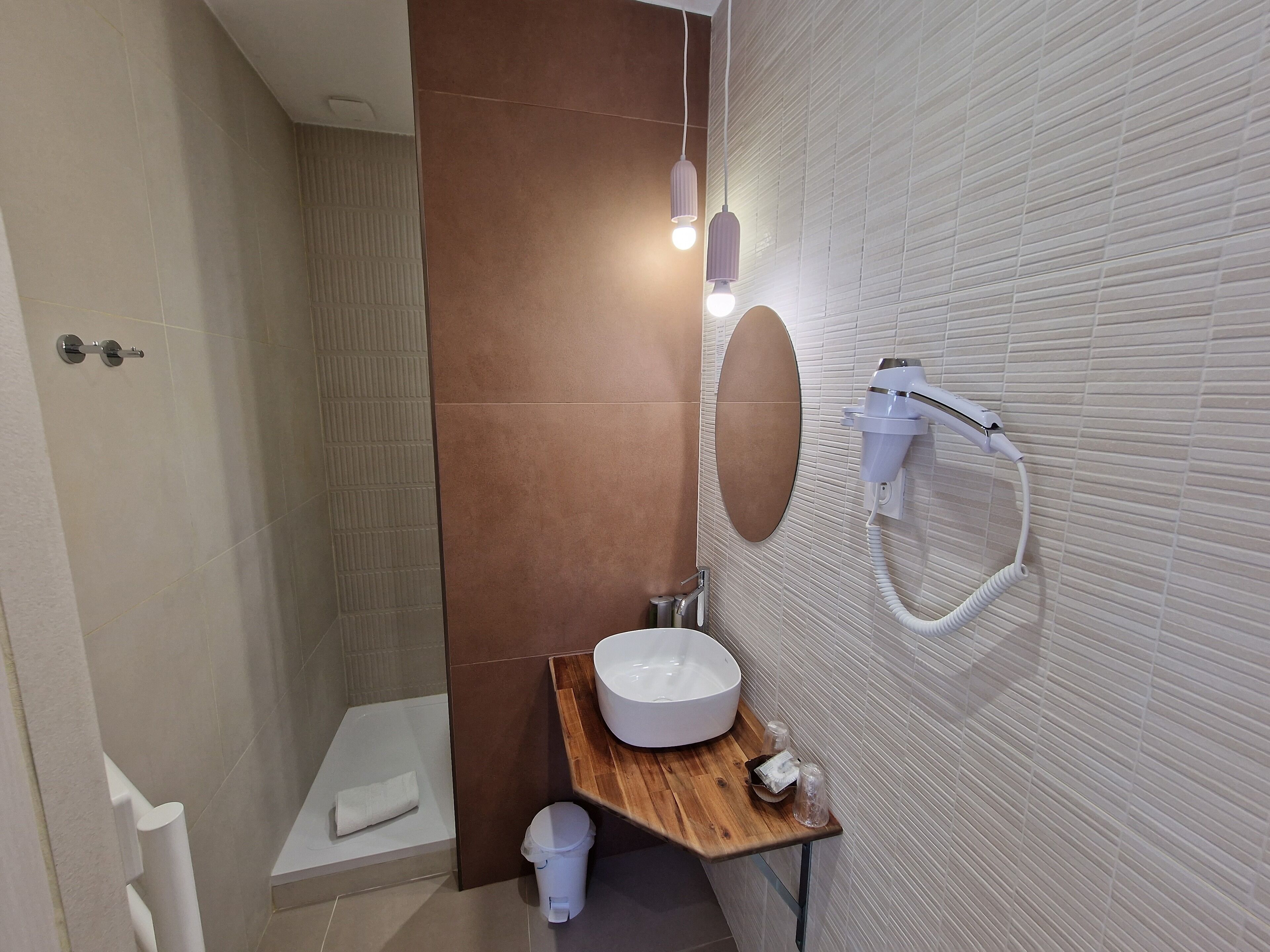 A modern bathroom with a wooden vanity, a large mirror, a wall-mounted hairdryer, and a shower area.