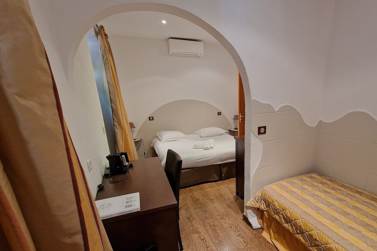 Una habitación de hotel con una cama, un escritorio con cafetera y una pequeña mesa.