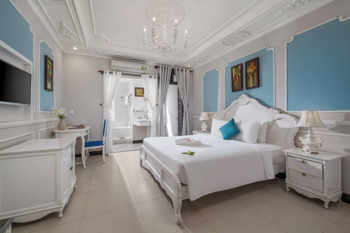 A bedroom with a large bed, white nightstands, a TV, and a bathroom with a shower and toilet.