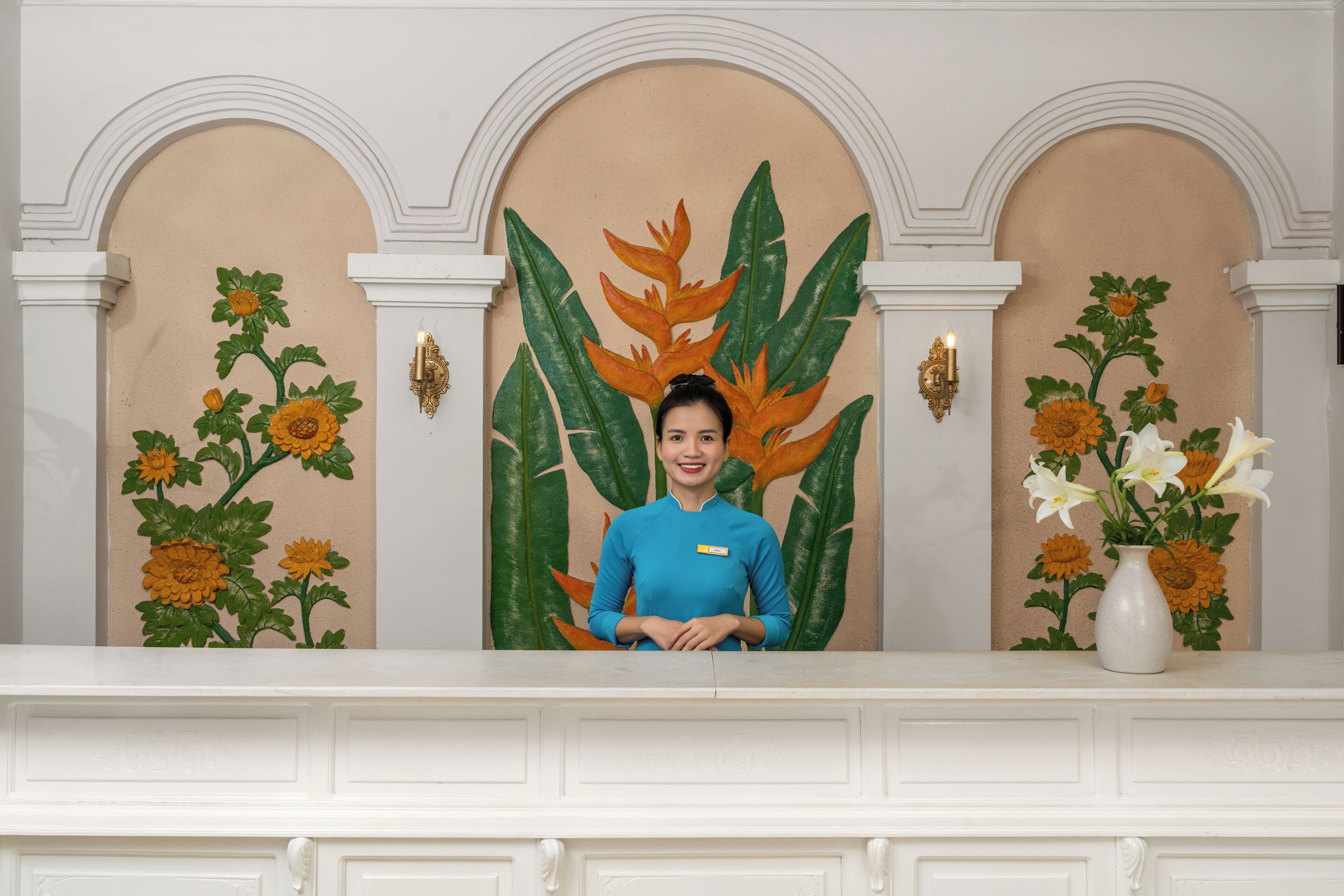 A reception area with a receptionist, a white reception desk, and a wall with floral artwork.