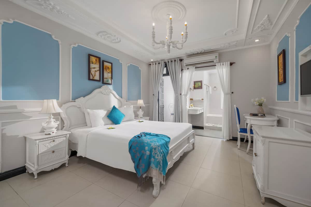A bedroom with a large bed, white nightstands, a dresser, a vanity, and a television.