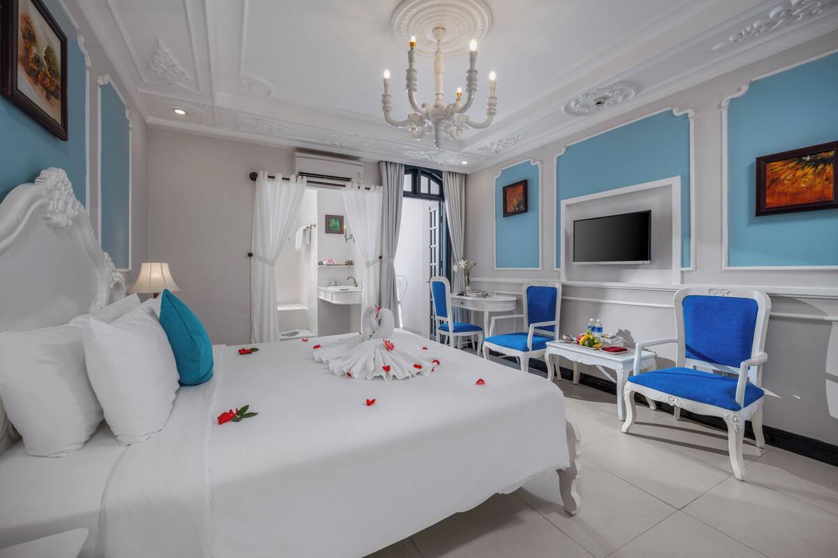 A hotel room with a large bed, a TV, a dining area, and a bathroom.