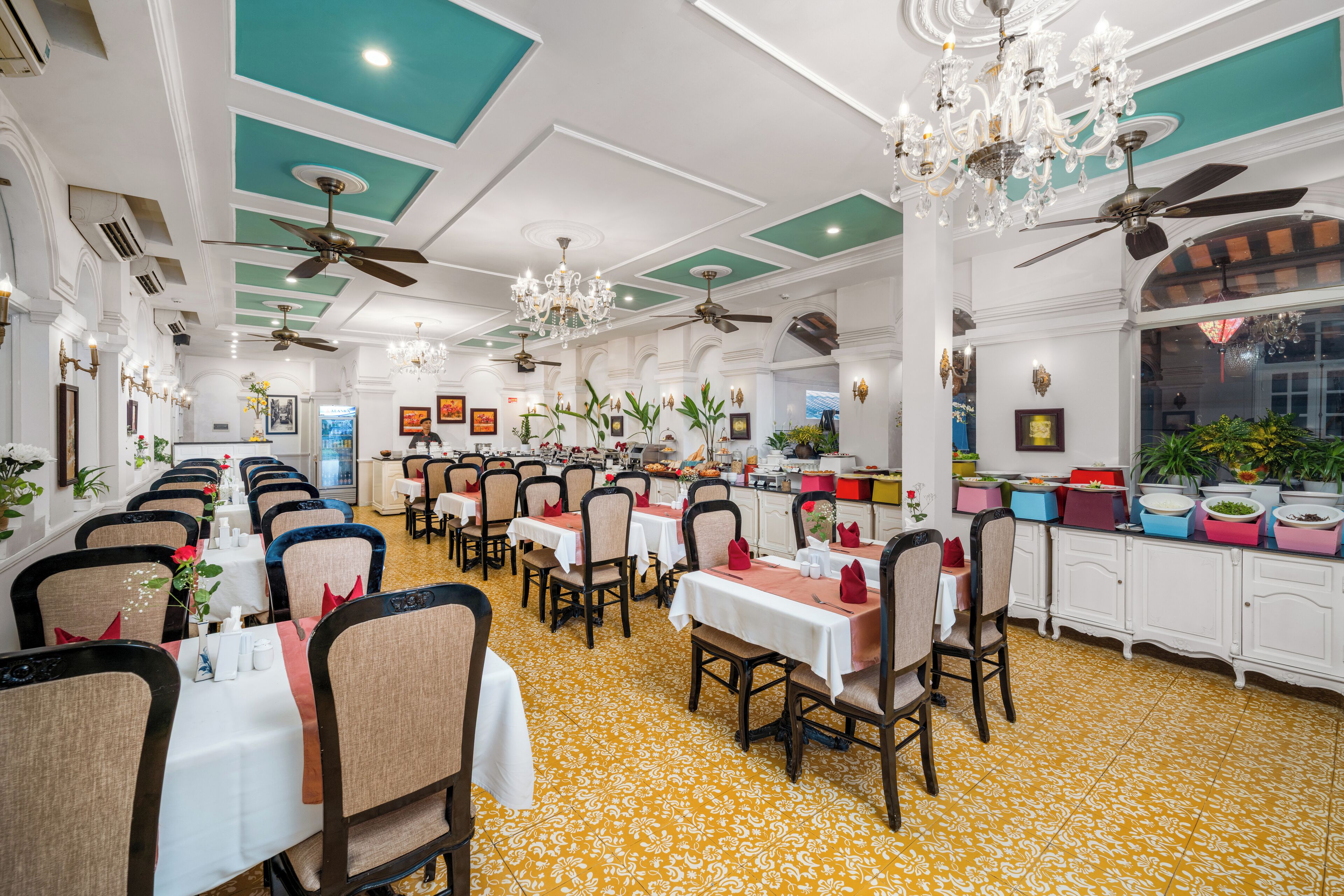 Un restaurante con varias mesas, sillas, ventiladores de techo, candelabros y plantas en macetas.
