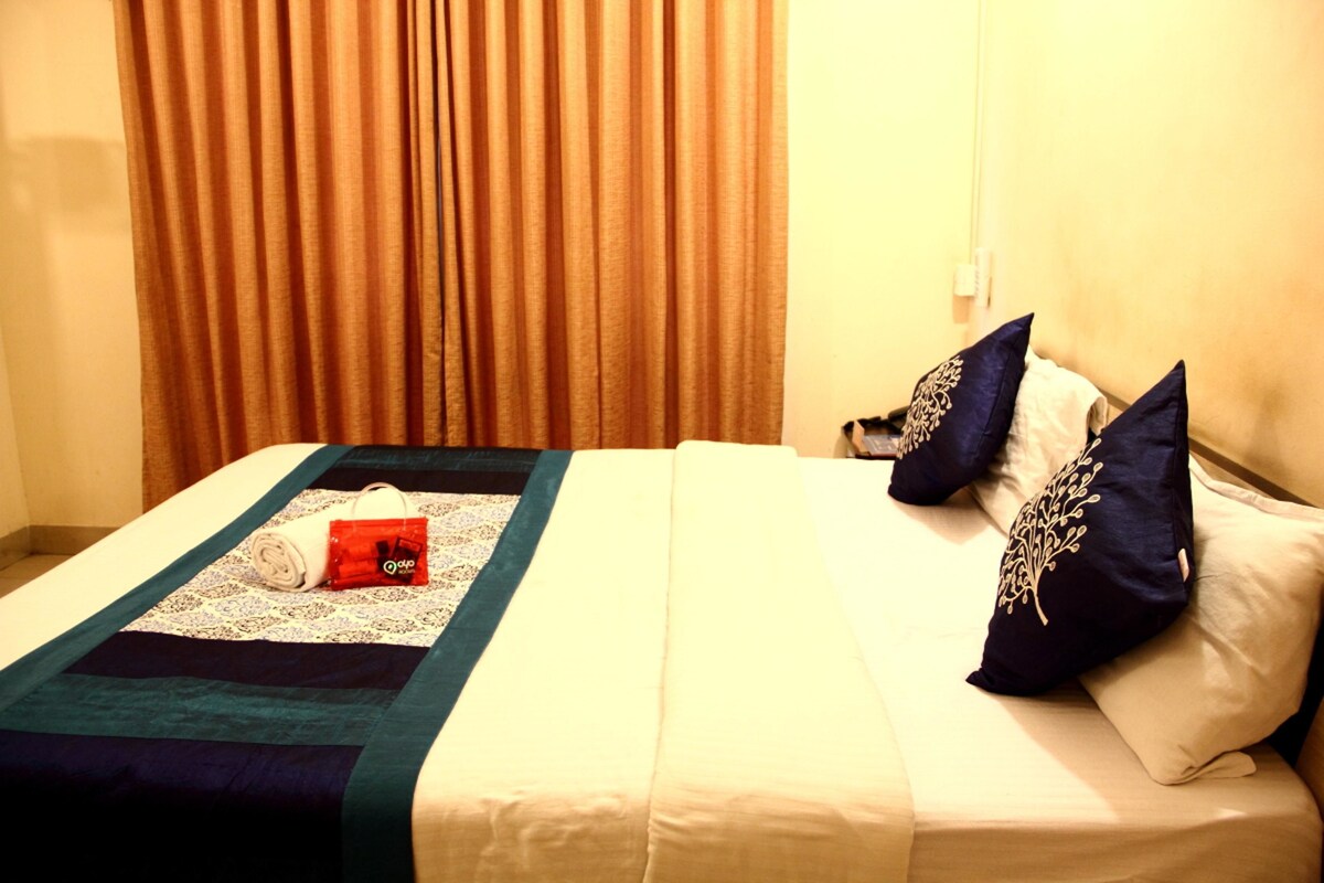 A hotel room with a neatly made bed, a rolled white towel, and a red object on the bed.
