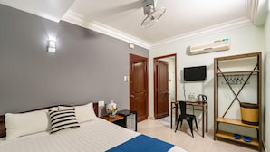 Habitación de hotel con una cama, un escritorio, una silla, un televisor y una estantería con una cesta.