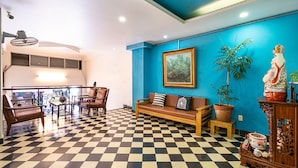 Un suelo a cuadros, un sofá, sillas, una mesa, una planta en maceta, una estatua y un cuadro en una habitación con paredes azules.