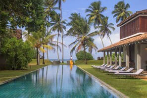 A swimming pool with lounge chairs, palm trees, and a building with a tiled roof. - The Frangipani Tree By Edwards Collection (Unawatuna)