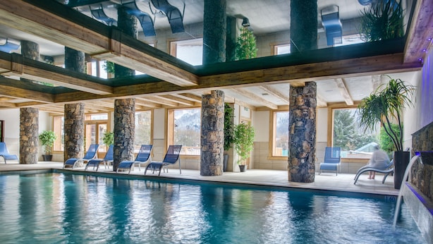 An indoor swimming pool with stone pillars, blue lounge chairs, and large windows. -  CGH Résidence Boutique les Chalets de Laÿssia (Samoëns)