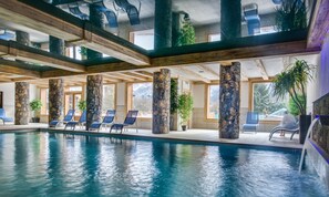 Una piscina interior con pilares de piedra, sillones reclinables azules y ventanas grandes.