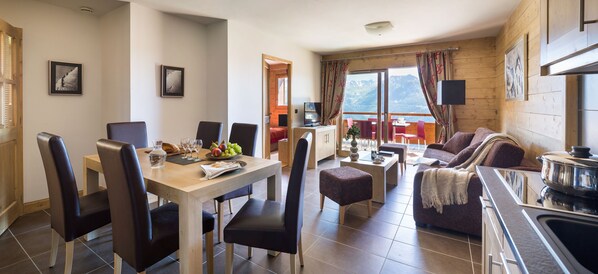 Una sala de estar moderna con comedor, cocina y balcón con vistas a las montañas.