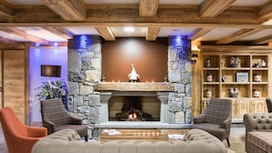 A cozy living room with a stone fireplace, wooden beams, and comfortable seating. -  CGH Résidence Boutique les Chalets de Laÿssia (Samoëns)
