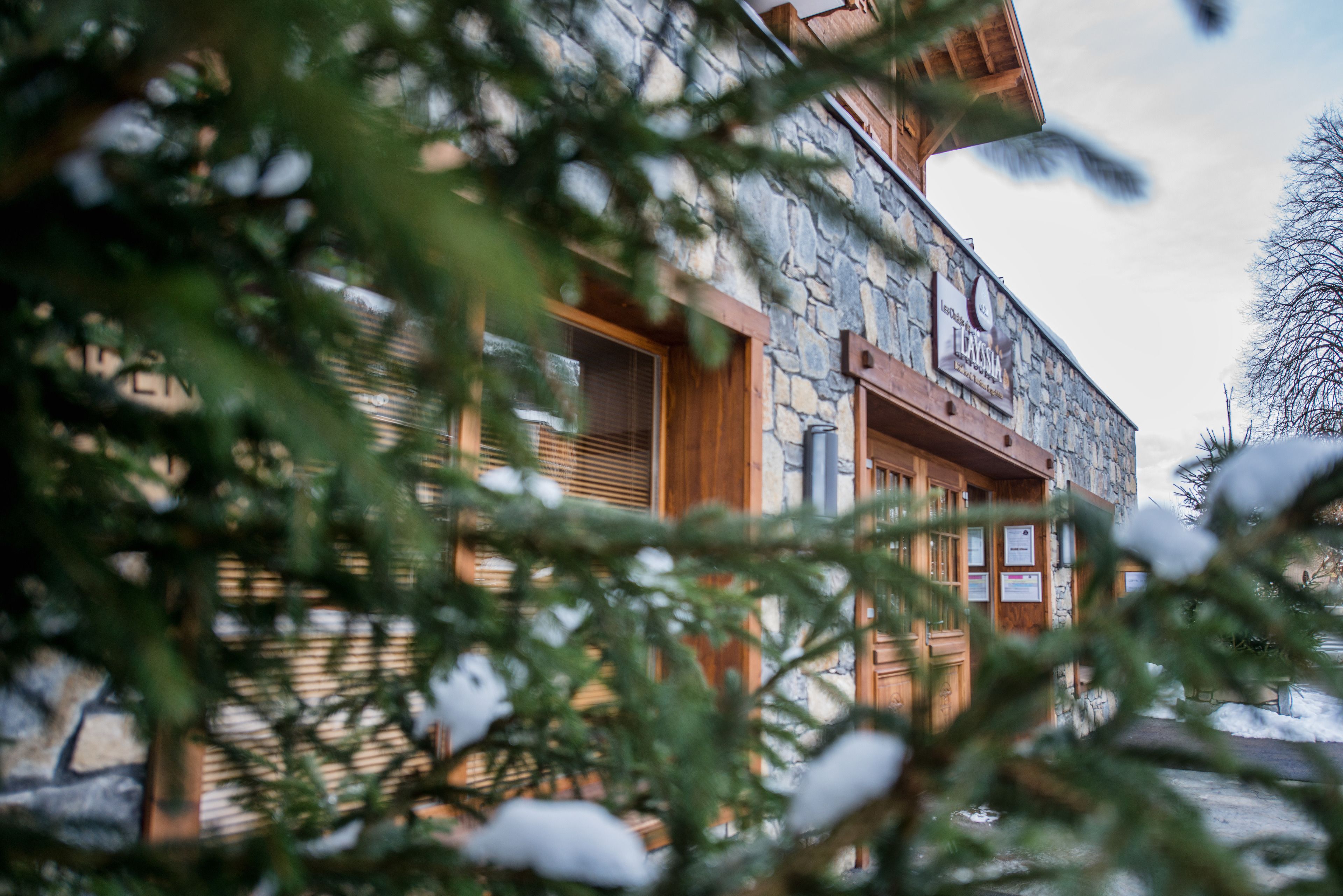A stone building with wooden doors and windows, surrounded by snow and trees.