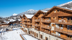 A multi-story wooden lodge with balconies, a stone facade, and a snow-covered ground. -  CGH Résidence Boutique les Chalets de Laÿssia (Samoëns)