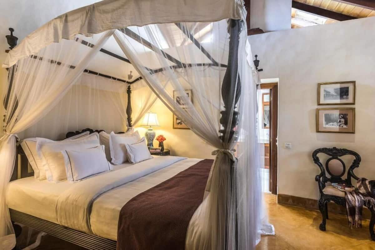 Ein Himmelbett mit weißer Bettwäsche und einer braunen Tagesdecke.