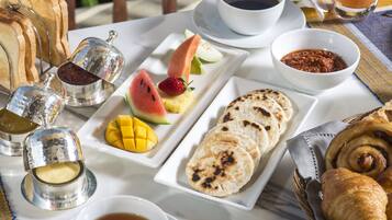 Un desayuno con tostadas, fruta, pasteles y bebidas sobre una mesa.