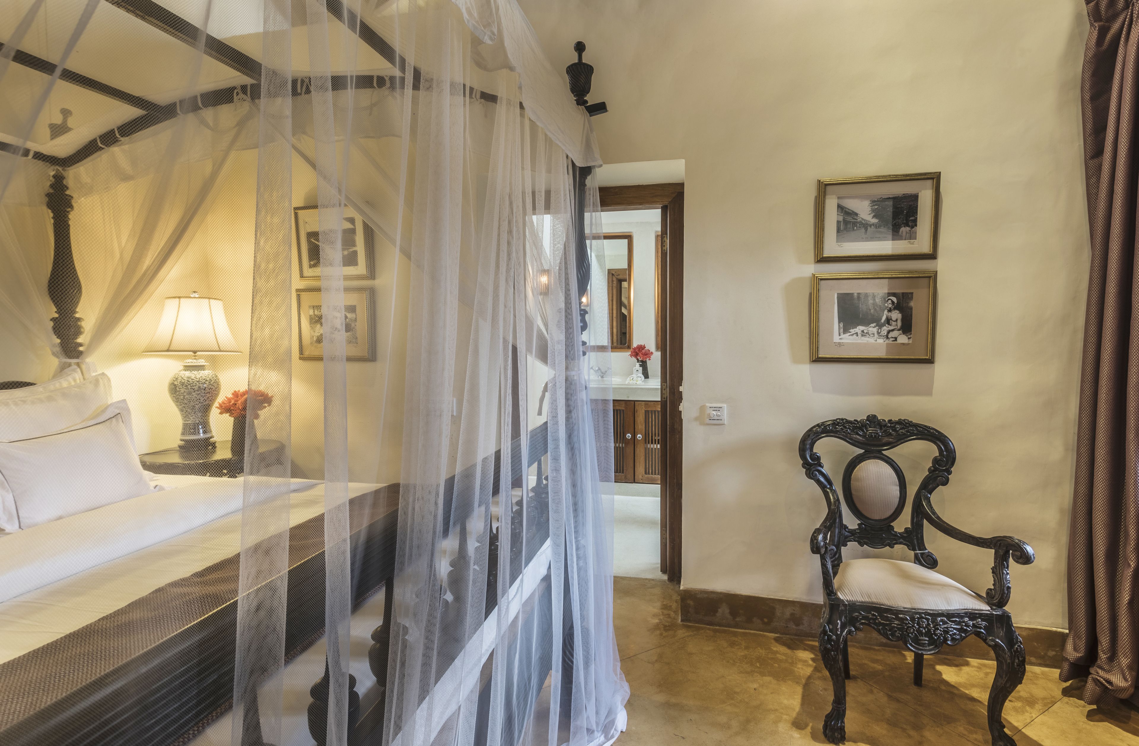 A bedroom with a four-poster bed, a bedside table with a lamp, and a chair.
