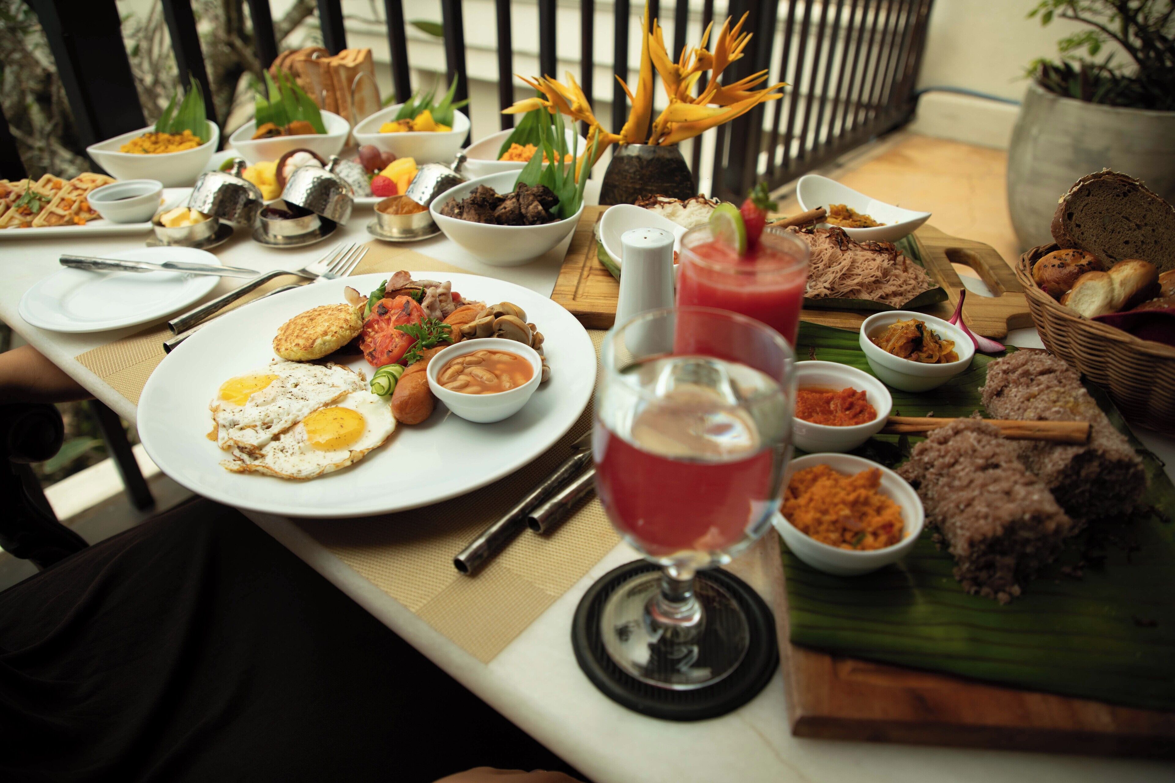 A table set with various dishes, including fried eggs, rice, and bread, along with condiments and a drink.