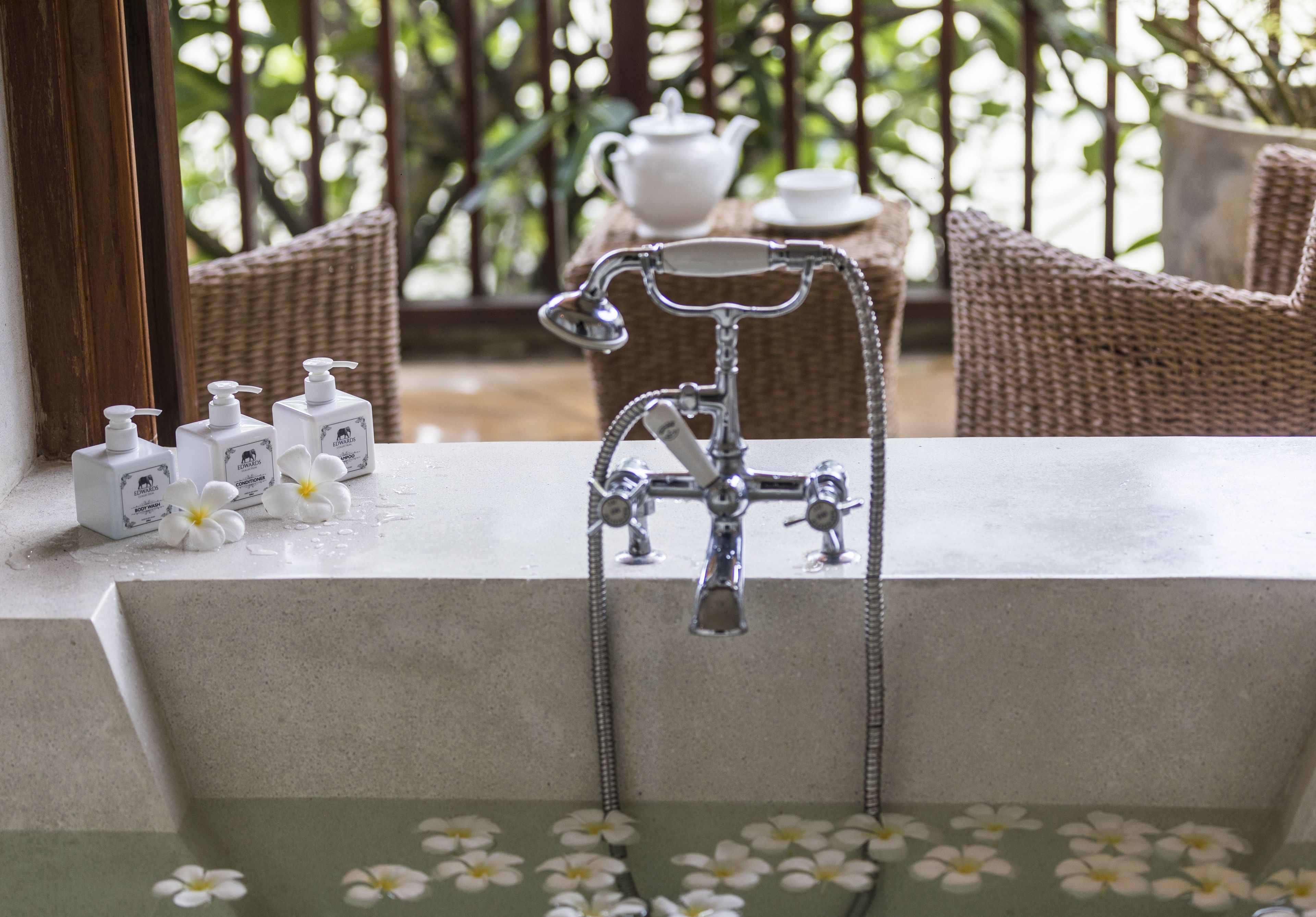 A bathroom with a modern faucet, a tea set, and toiletries on the counter.