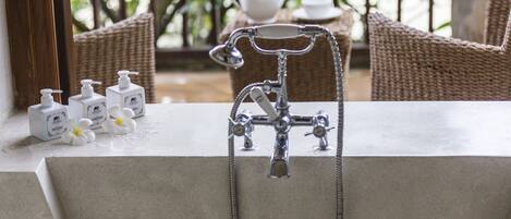 Une salle de bain dotée d’un robinet moderne, d’un service à thé et de produits de toilette posés sur le comptoir.