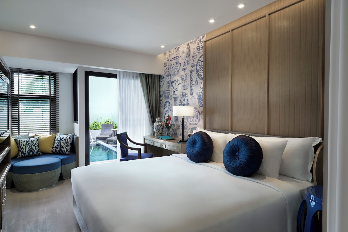 Una habitación de hotel moderna con una cama grande, un escritorio, una silla y vistas a la piscina.
