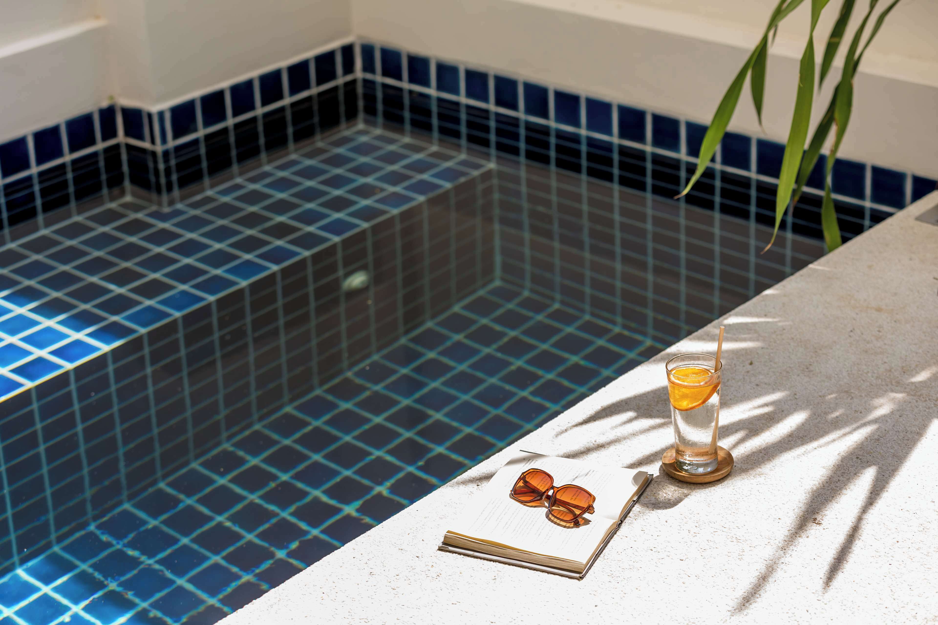Une zone autour d’une piscine carrelée, avec un verre et des lunettes de soleil posés sur une surface blanche.