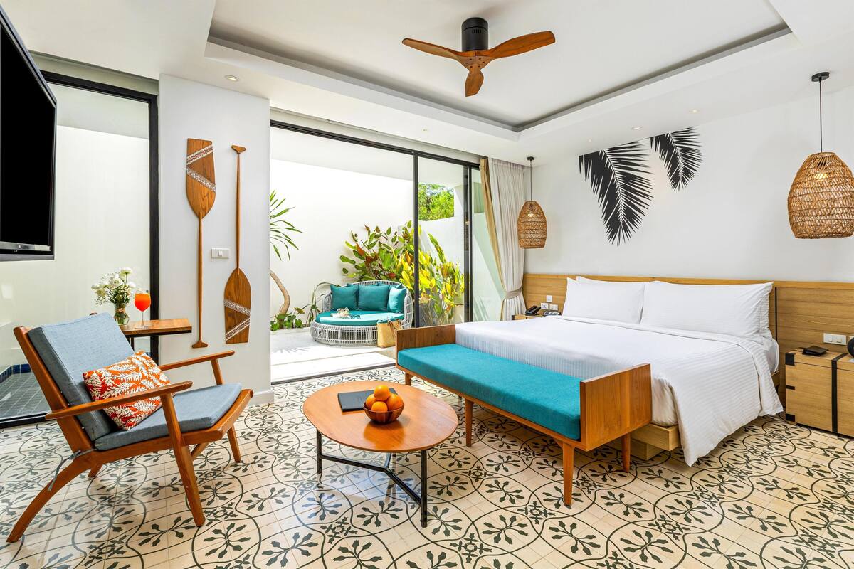 Habitación de hotel con cama, sofá, sillón, una pequeña mesa con fruta y vistas al exterior.