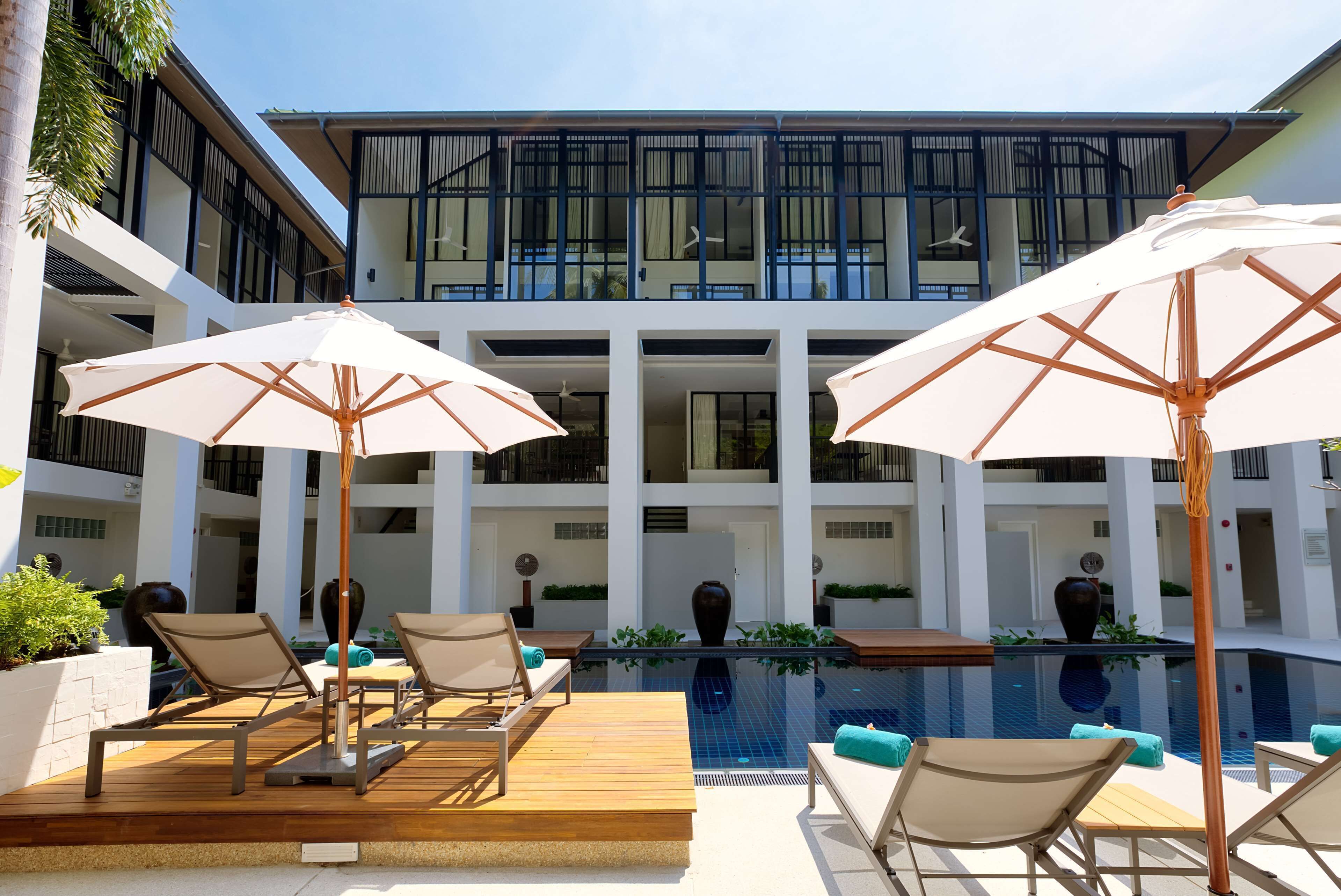 A poolside area with lounge chairs and umbrellas, a modern building in the background, and a clear sky.