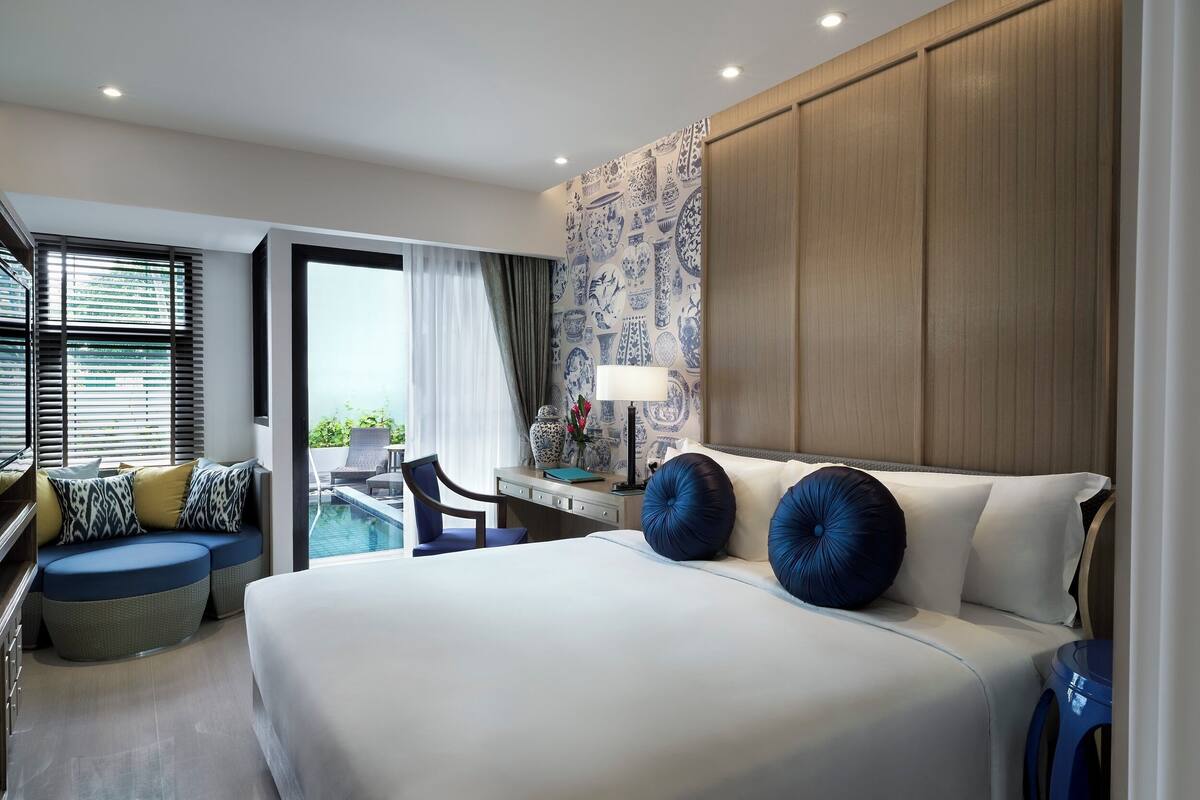Una habitación de hotel moderna con una cama grande, un escritorio, una silla y vistas a la piscina.