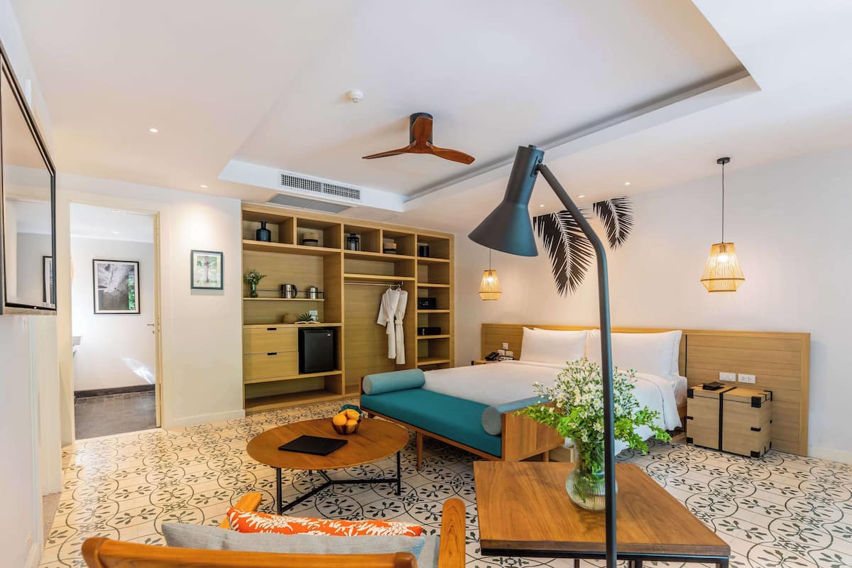 Una habitación de hotel con cama, escritorio, silla, estantería, armario y ventilador de techo.