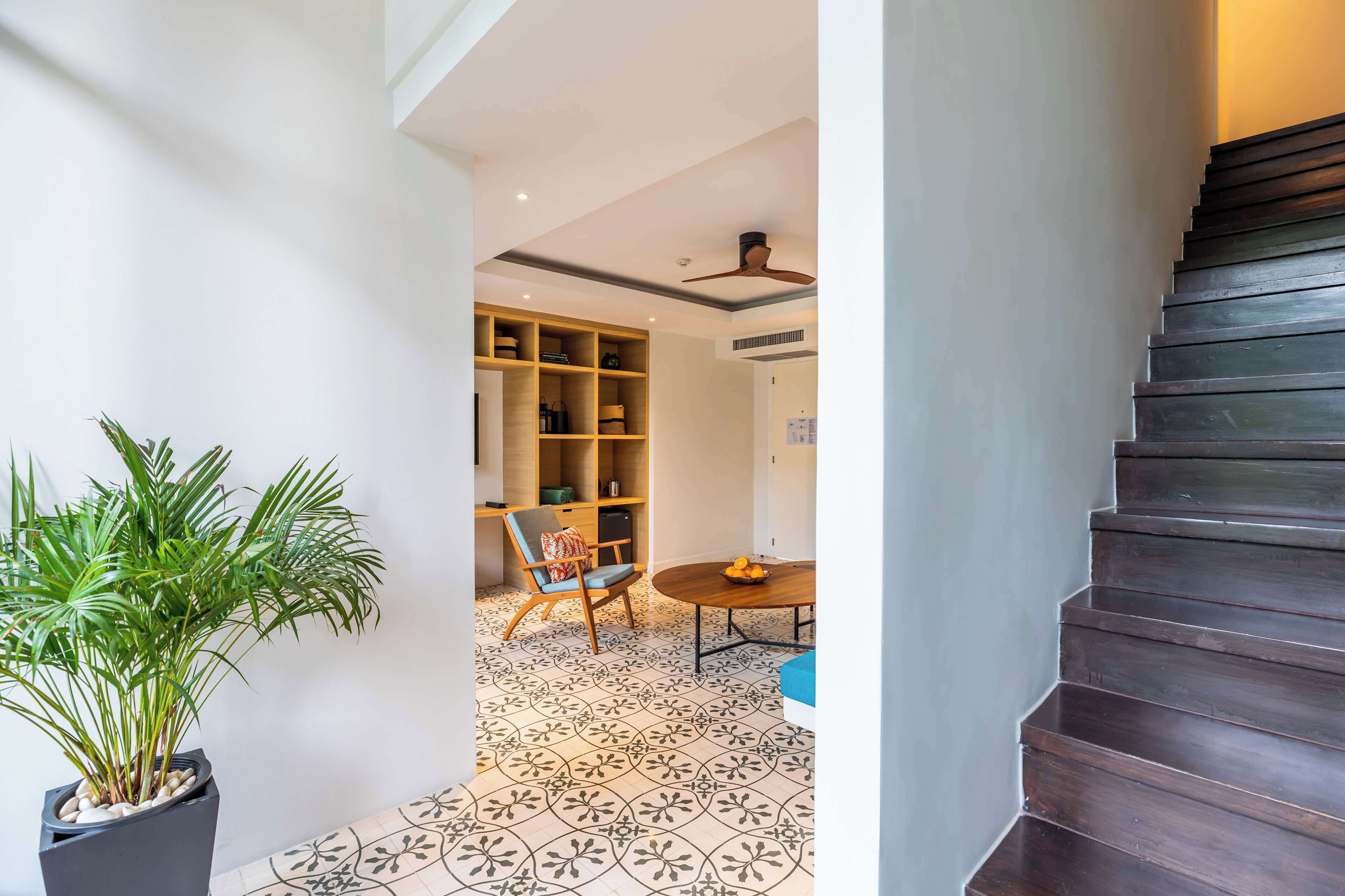 A staircase leading to a room with a patterned floor, a potted plant, a chair, a table, and a bookshelf.