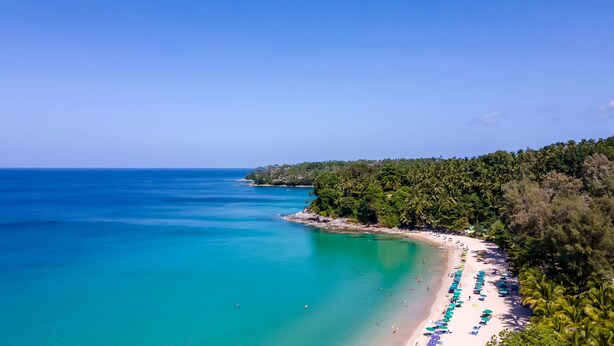 A coastal beach with clear turquoise waters, a sandy shoreline, and dense tropical vegetation. - OUTRIGGER Surin Beach Resort (Choeng Thale)