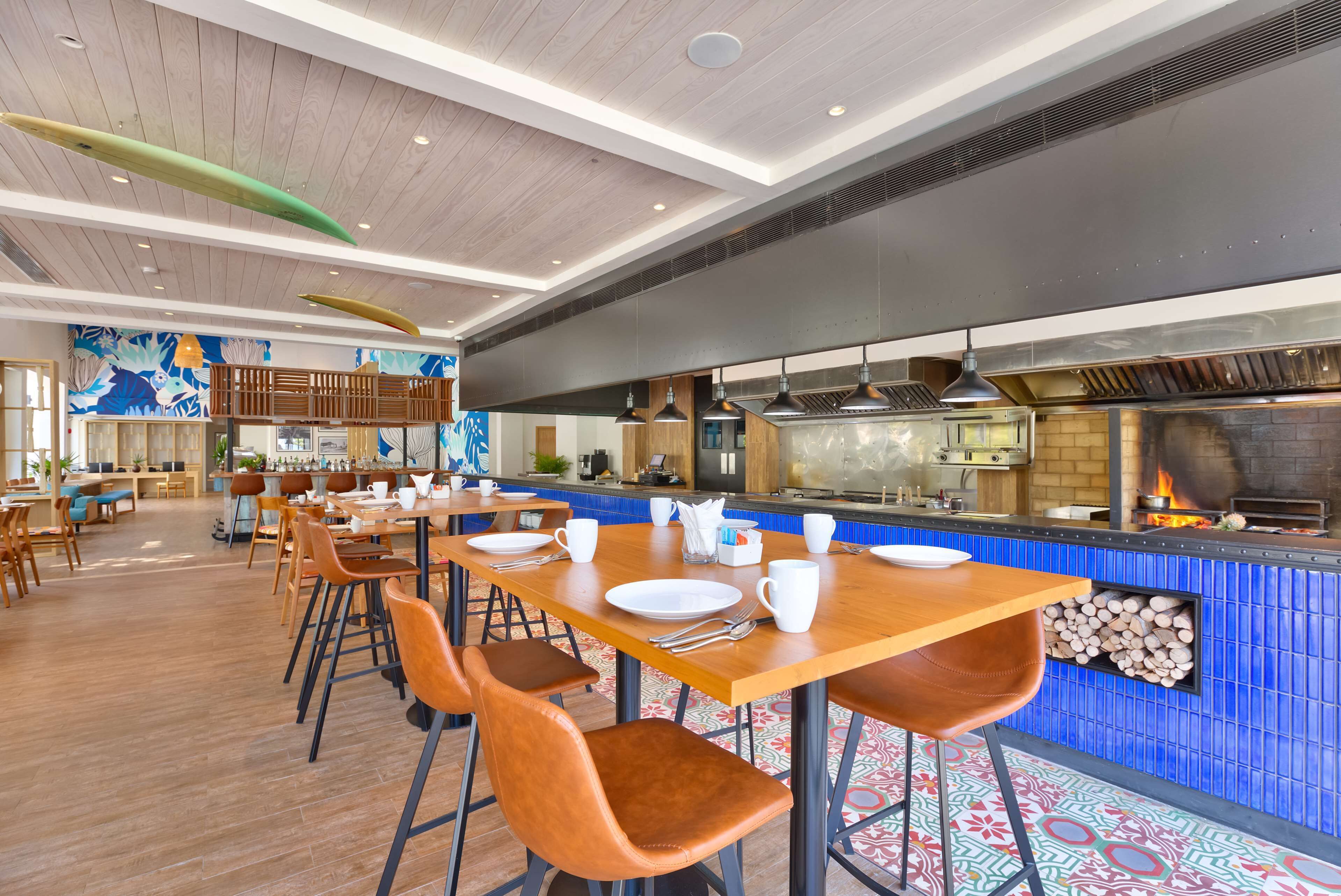 A restaurant with wooden tables and chairs, a kitchen area, and a decorative ceiling.