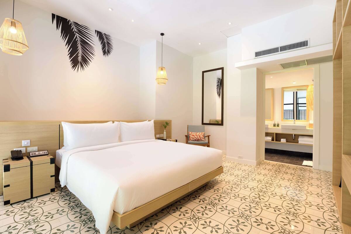 Habitación de hotel con una cama grande, mesitas de noche, un tocador, un espejo y un baño visible a través de una puerta abierta.