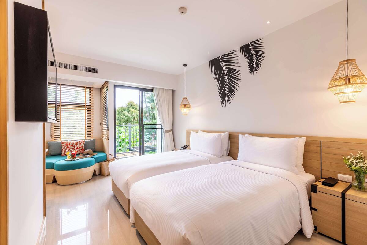 Habitación de hotel con dos camas, un sofá, un televisor y un ventanal grande con persianas.
