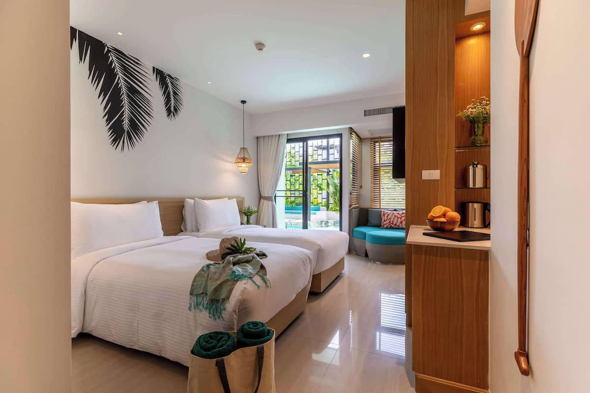 Habitación de hotel con cama, zona de estar, aparador de madera y vistas al exterior.