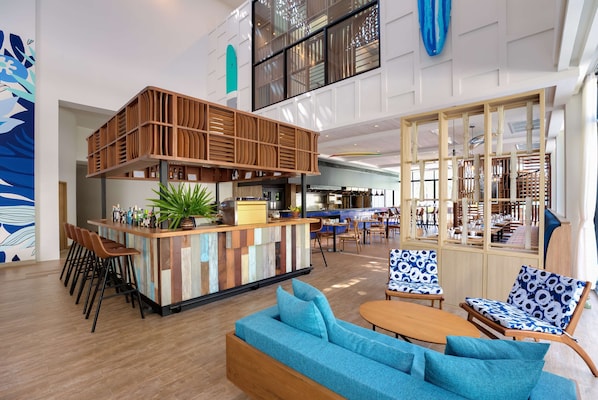 A modern bar area with a wooden counter, seating with blue cushions, and a large window. - OUTRIGGER Surin Beach Resort (Choeng Thale)