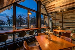 A restaurant with large windows, wooden tables, and chairs.