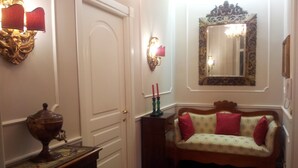 A hallway with a white door, a small table with a decorative urn, a sofa with patterned cushions, and a mirror with an ornate frame. - Romebest (Rome)