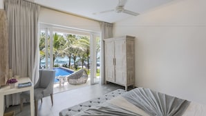 Une chambre avec un lit, un bureau, une chaise, une armoire et une vue sur une piscine et des palmiers.