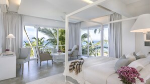 Une chambre moderne avec un grand lit, un coin salon avec des fauteuils et une vue sur l’océan.