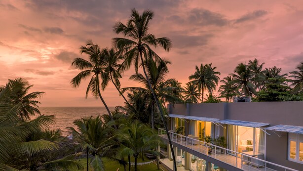 Un hôtel moderne doté d’une piscine, d’un espace extérieur aménagé et offrant une vue sur l’océan au coucher du soleil.