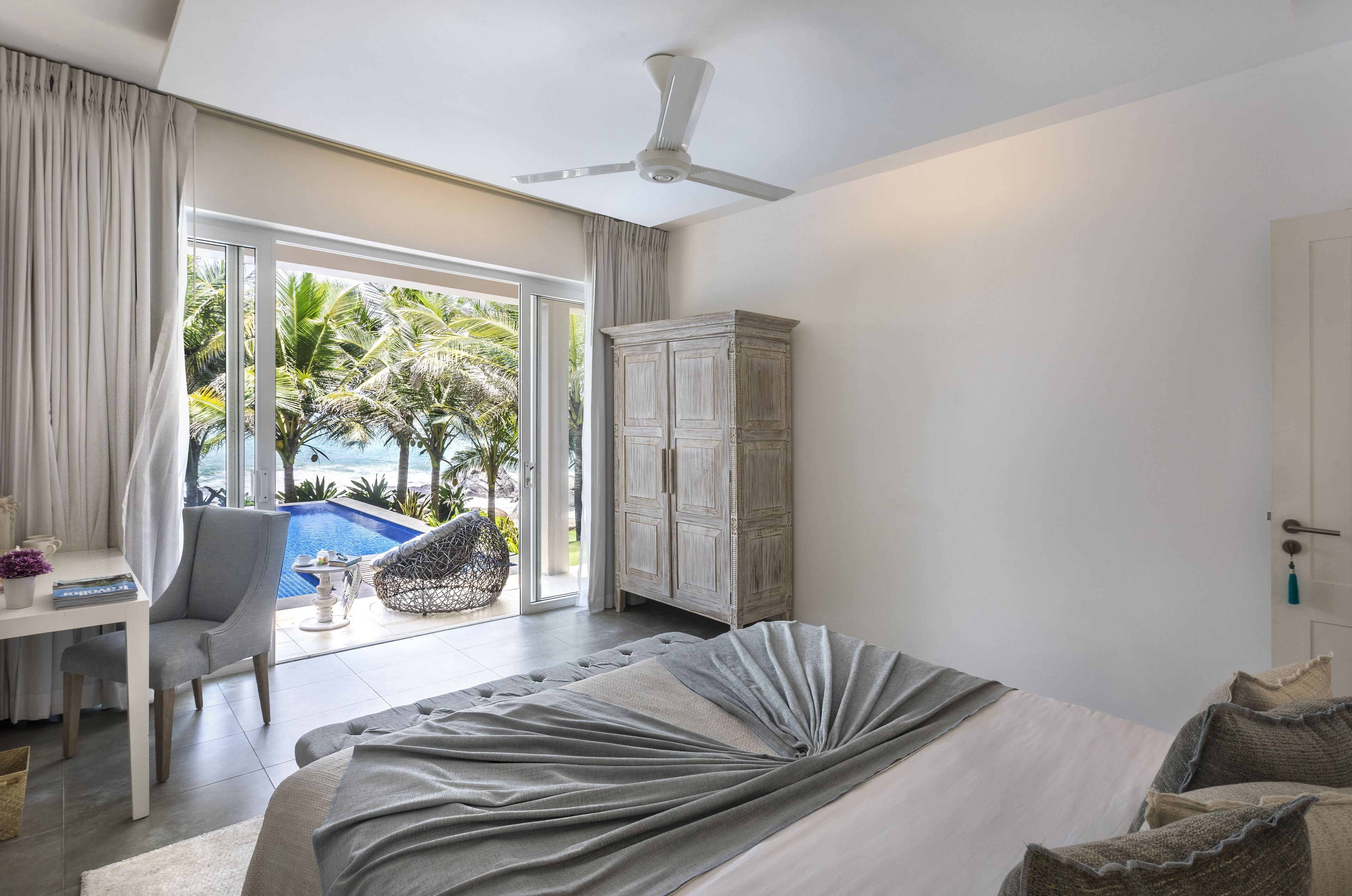 A bedroom with a bed, a desk, and a view of a pool and palm trees.