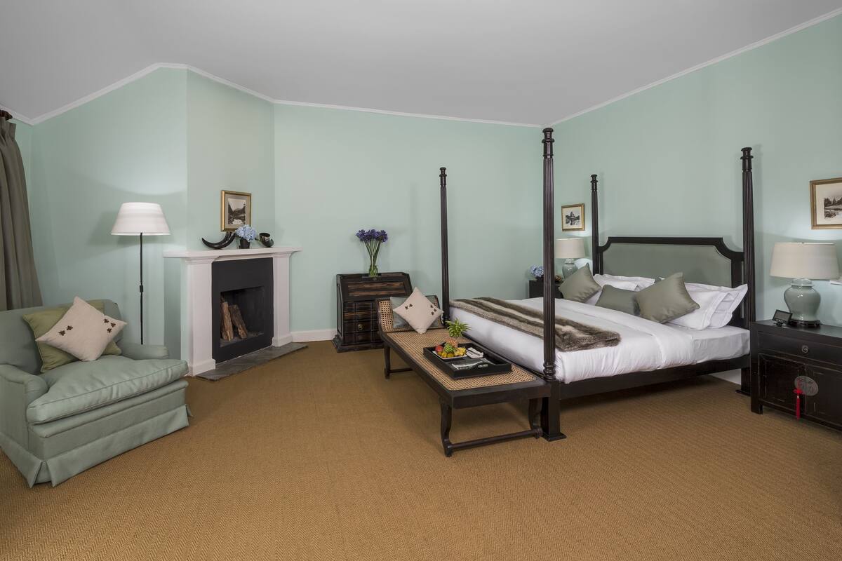 A four-poster bed with a nightstand, a sofa, a fireplace, and a window with curtains.