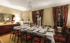 A dining room with a long table set for a meal, surrounded by wooden chairs with red cushions.