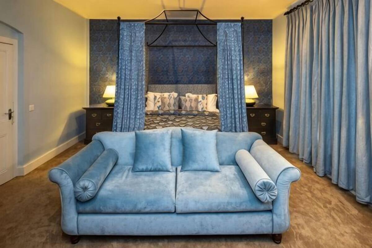 A room with a blue sofa, a bed with patterned bedding, and curtains.