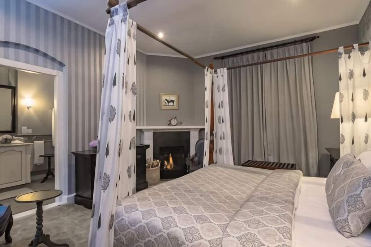 A bedroom with a four-poster bed, a fireplace, a bedside table, and a mirror.