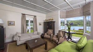 A living room with a sofa, armchairs, a coffee table, and a view of a lake through large windows. - Hill Rise Luxury Villa & Stables by Edwards Collection (Nuwara Eliya)